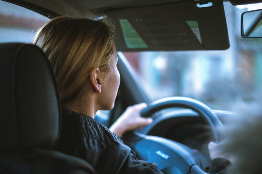 Jeune conductrice au volant d’une voiture, les deux mains sur le volant, vue depuis l’arrière de l’habitacle